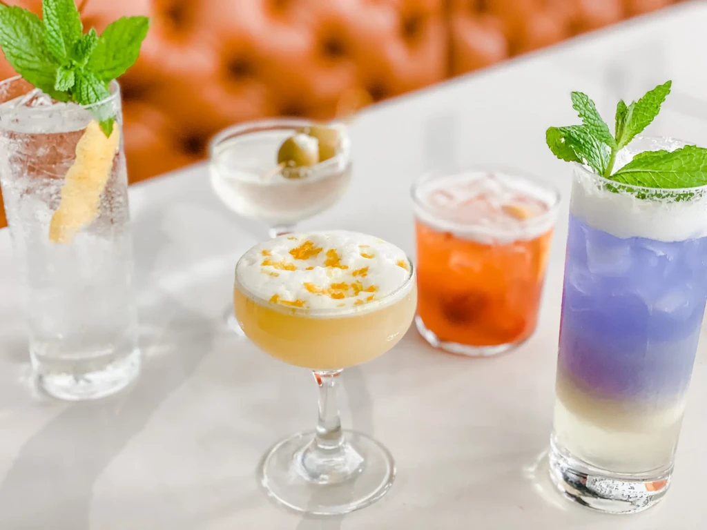 Five distinct cocktails, garnished, on a light bar surface.