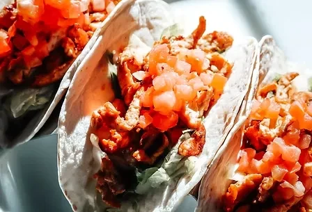 Three soft tacos with shredded meat, lettuce, and diced tomatoes, top-down.