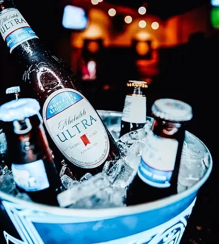 Cold Michelob Ultra beer bottles in an ice bucket at a blurred bar.