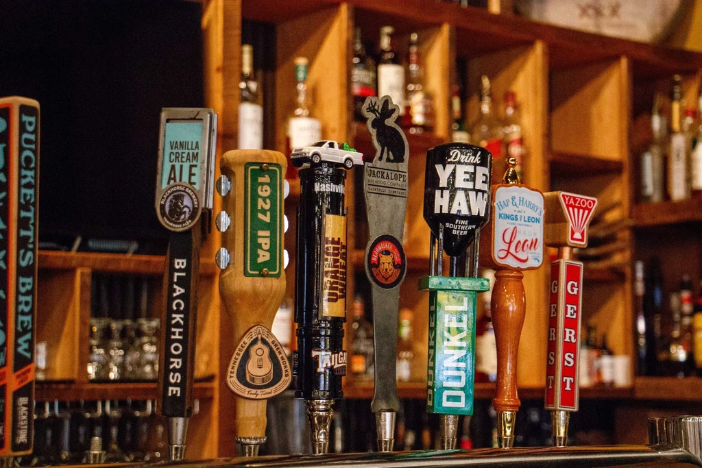 Close-up: Nine colorful, branded beer tap handles at a bar.