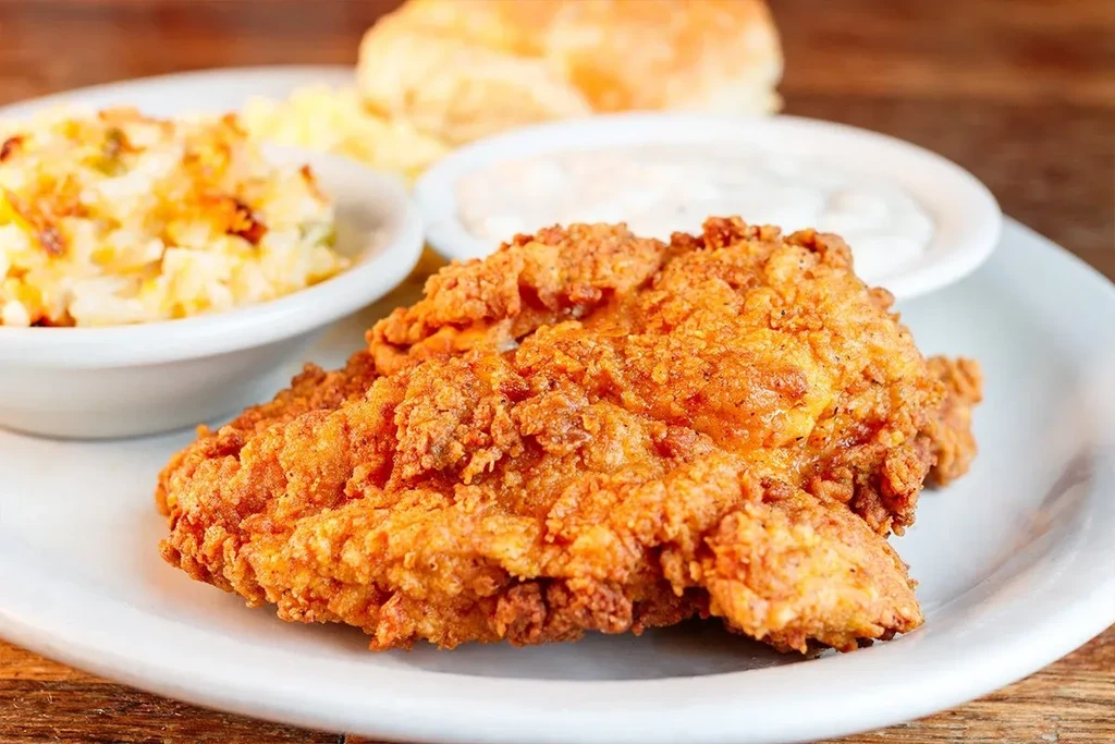 Crispy golden-brown fried chicken, coleslaw, sauce, and biscuit on wood.