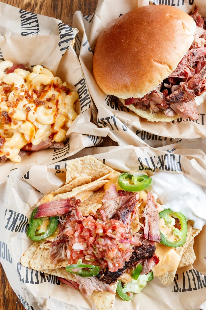 Three baskets of mac and cheese, BBQ sandwich, and loaded nachos.
