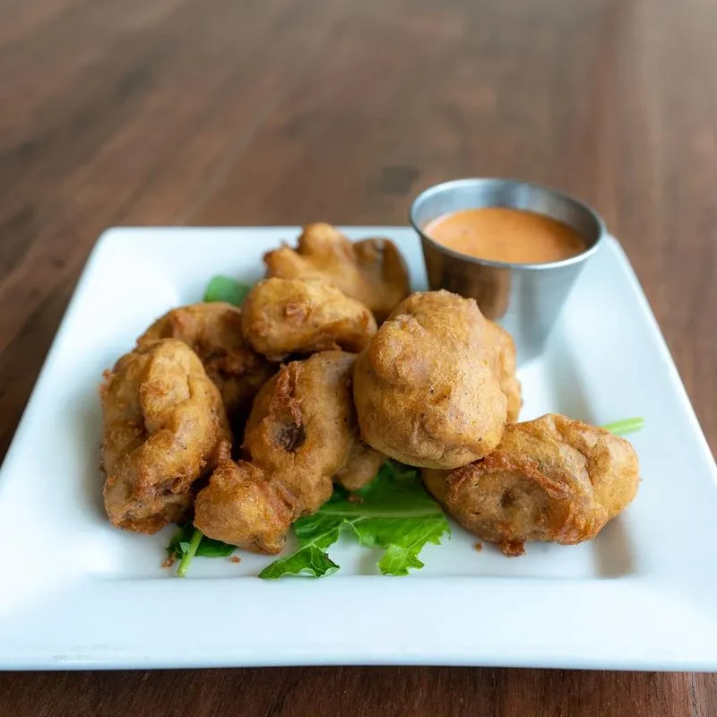 Crispy golden fritters, green garnish, and dipping sauce on a plate.
