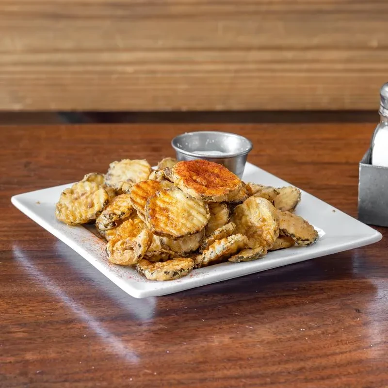 Golden fried pickle chips on a white plate with white dipping sauce.