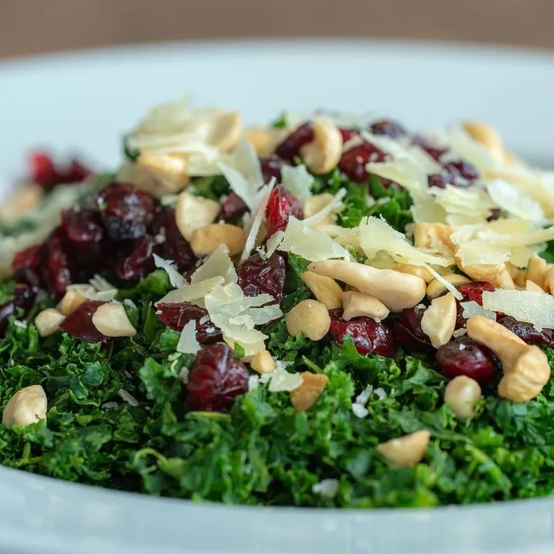 Close-up of kale salad with cranberries, cashews, and cheese shavings.