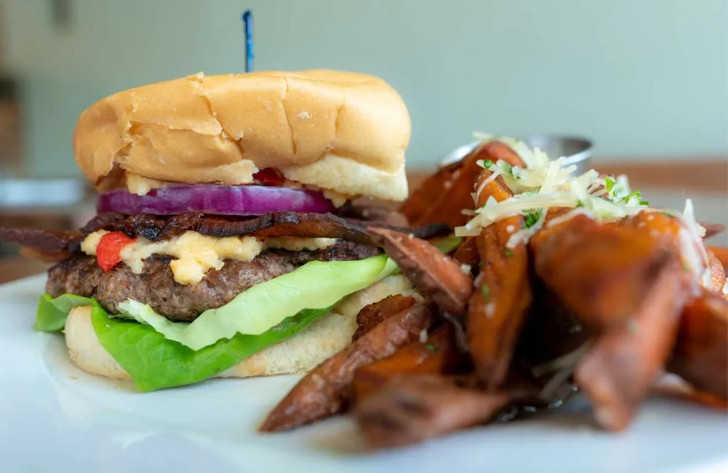 Gourmet burger with bacon, cheese, lettuce, and sweet potato fries.