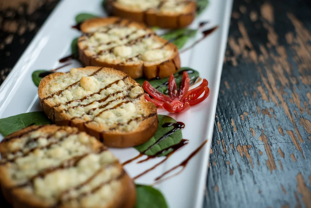 Five bruschetta with cheese, balsamic glaze, spinach on a white plate.