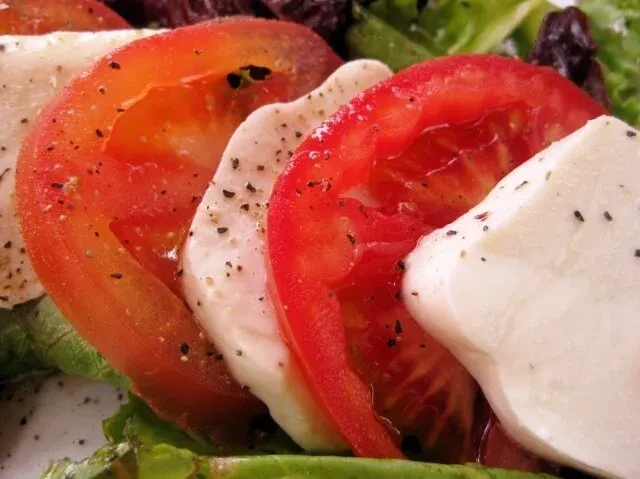 Alternating slices of red tomato, white mozzarella, and lettuce with pepper.
