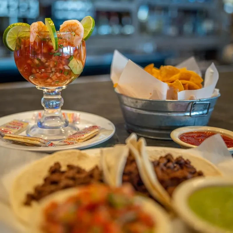 Mexican food spread with shrimp cocktail, tacos, chips, and salsa.