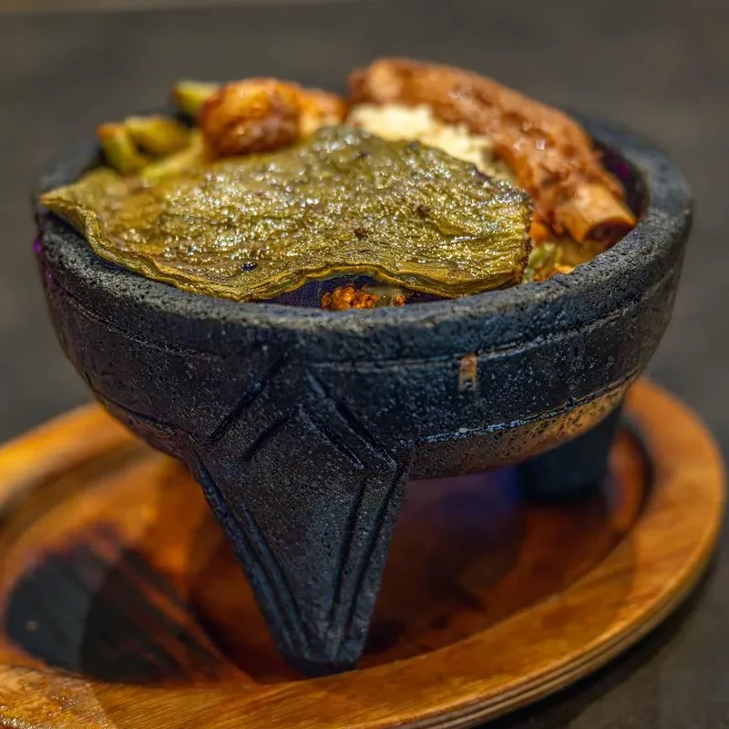 Blistered green chili and meat served in a molcajete on a wooden board.