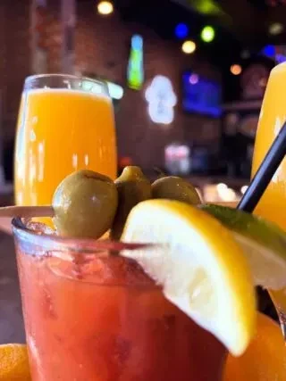Garnished Bloody Mary and orange juice in a blurred bar.
