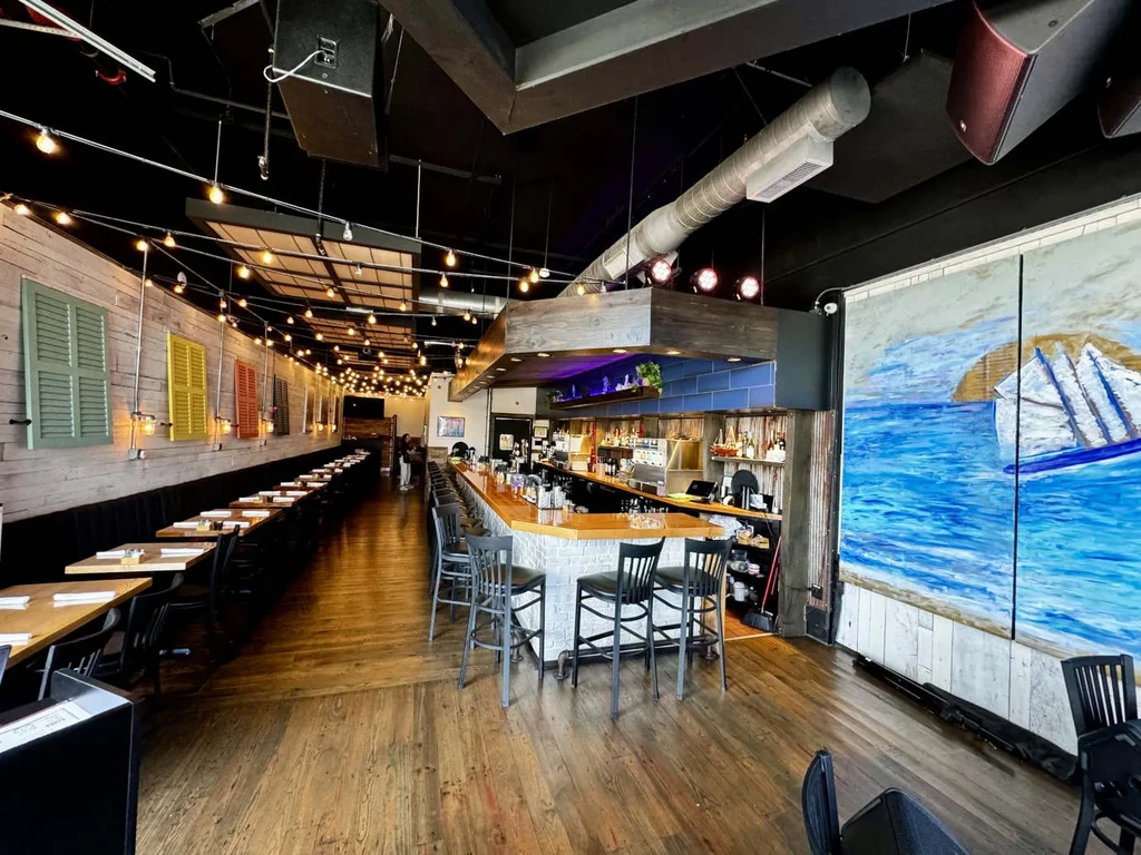 Warm, rustic restaurant interior with booth seating, bar, and ocean mural.