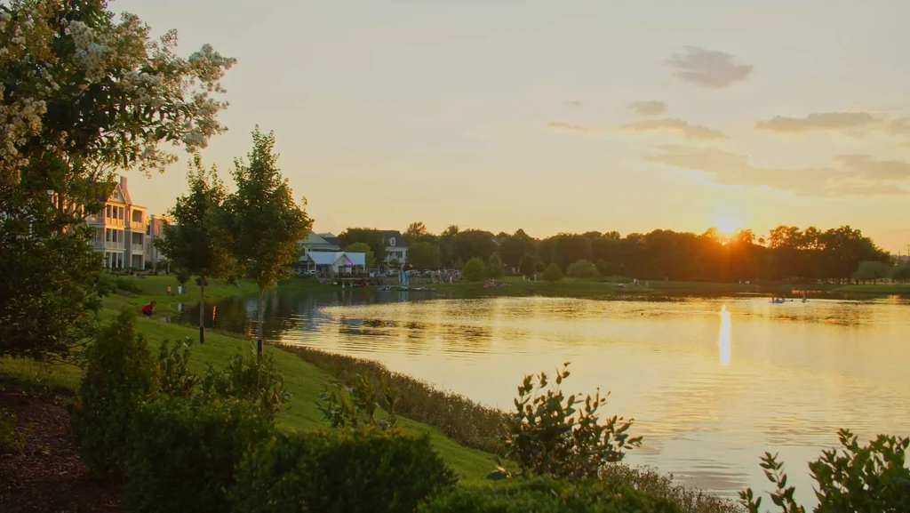 Golden sunset over water, with buildings, trees, and people visible.