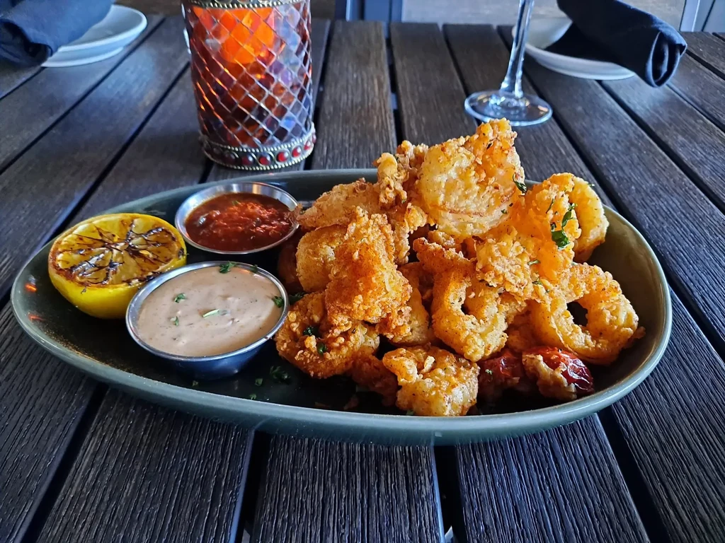 Crispy golden fried seafood, sauces, grilled lemon, rustic setting.