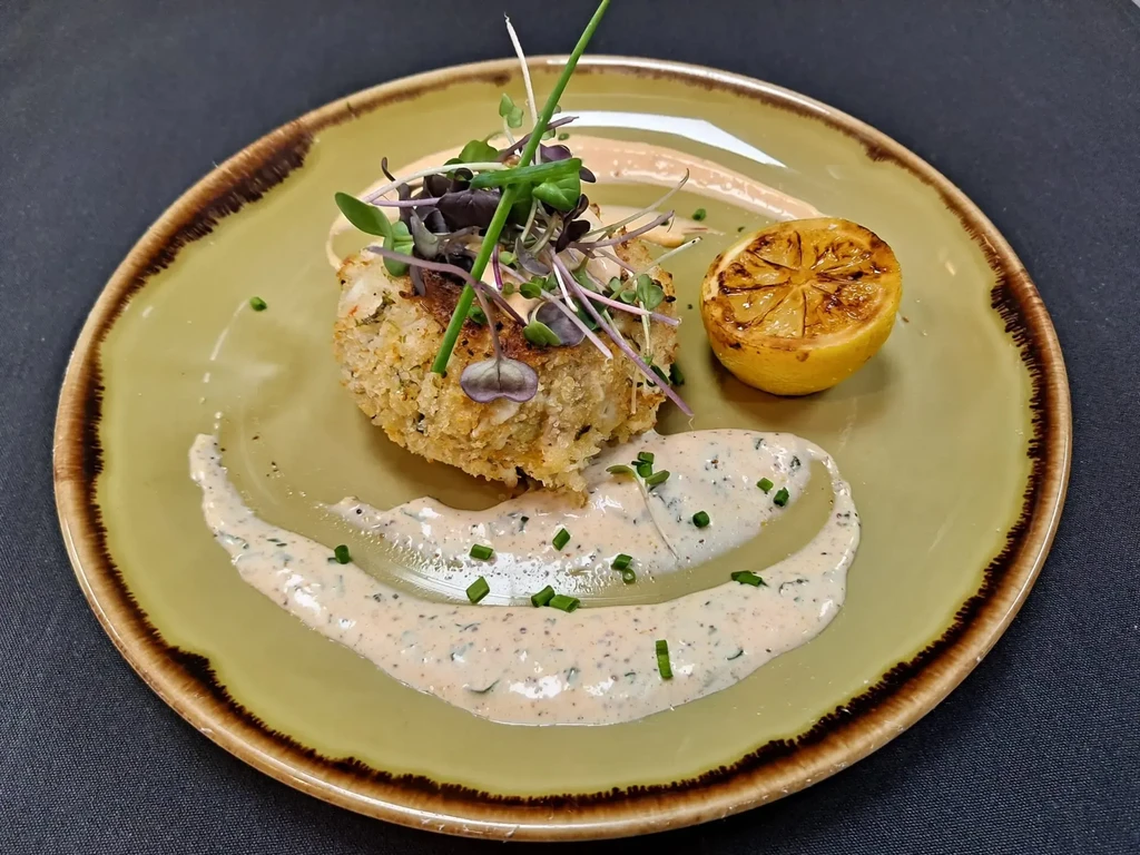 Crispy golden patty, microgreens, grilled lemon, chive sauce on rustic plate.