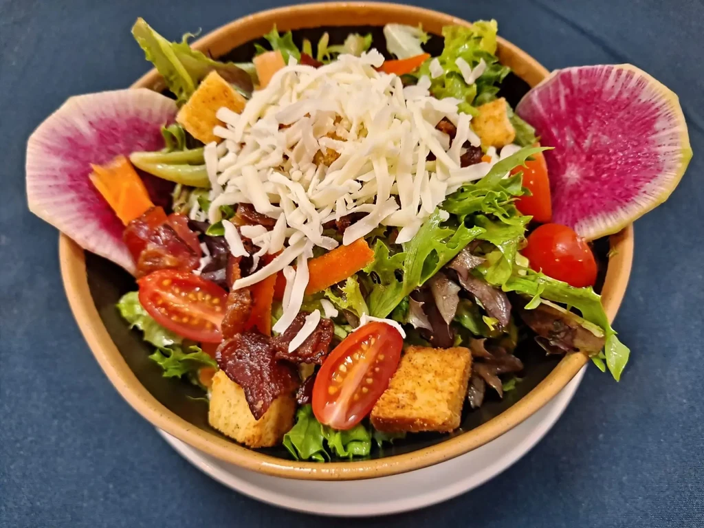 Vibrant salad topped with cheese, croutons, tomatoes, bacon, and radish.