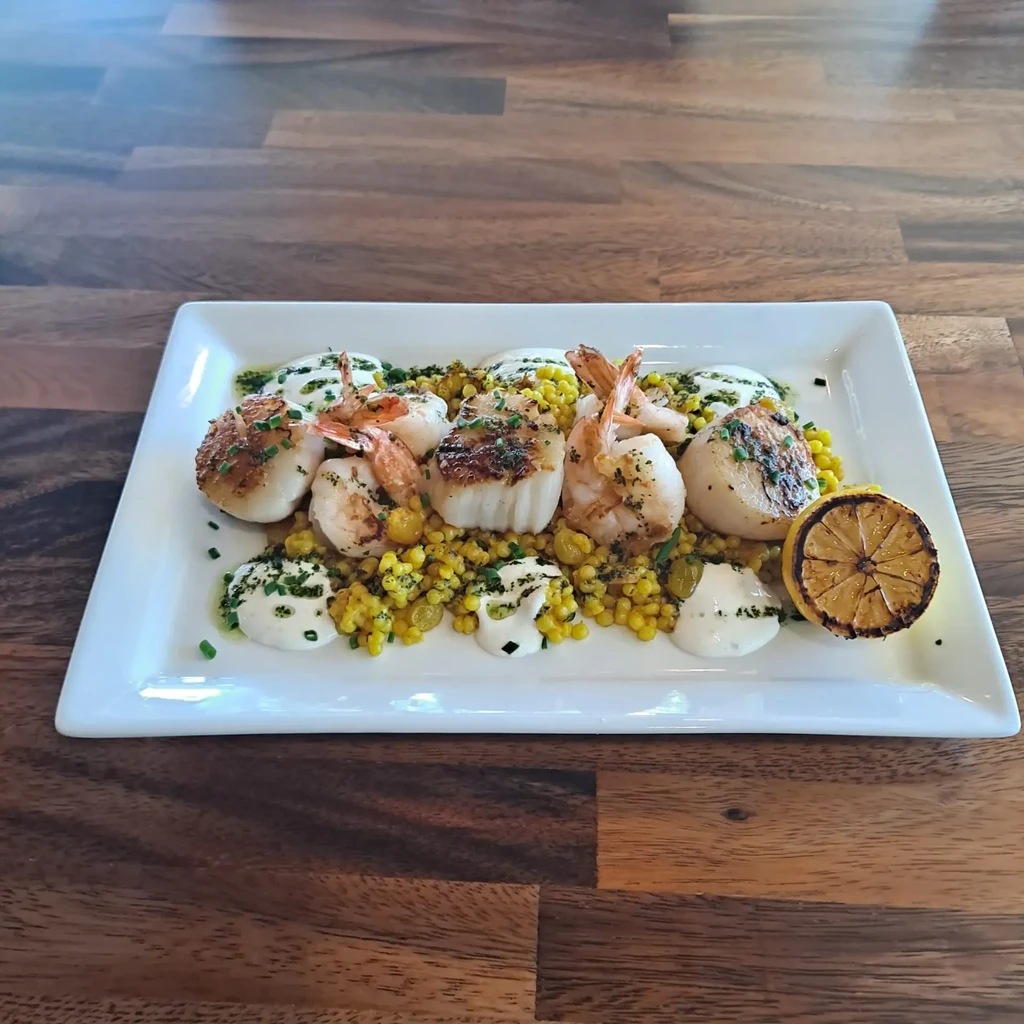 Seared scallops and shrimp on couscous with herbs, sauce, and lemon.