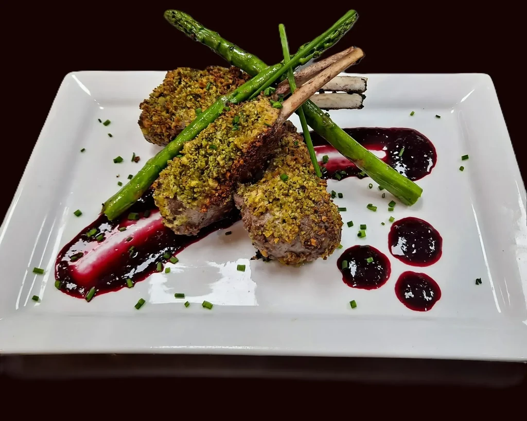 Three green-crusted lamb chops, asparagus, dark sauce, chives on plate.