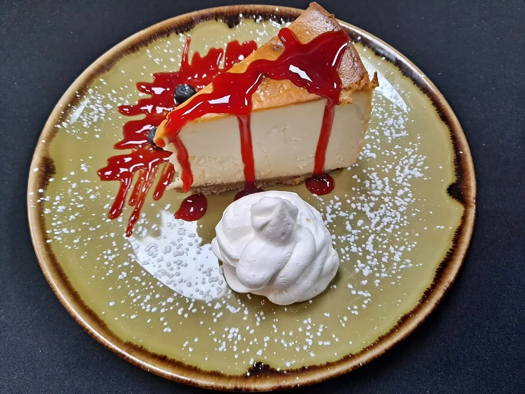 Cheesecake with red berry sauce, blueberries, whipped cream, and powdered sugar.