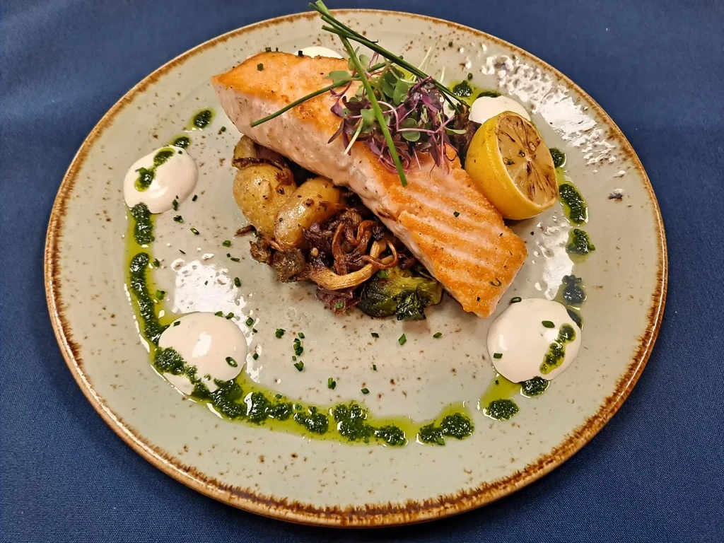 Plated salmon, roasted vegetables, charred lemon, and sauces.