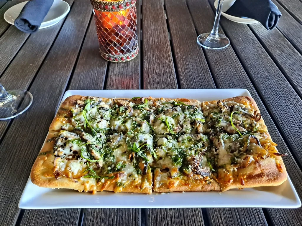 Rectangular flatbread with melted cheese, sautéed mushrooms, green sauce, and greens.
