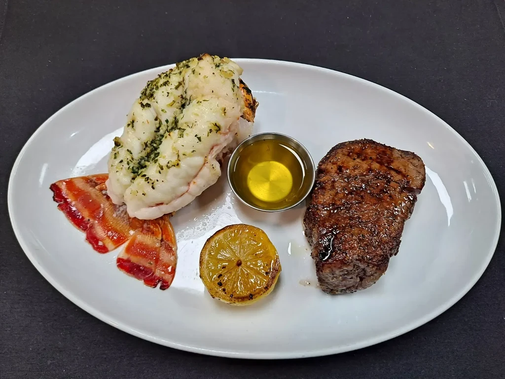 Plated surf and turf with lobster tail, grilled steak, and lemon.