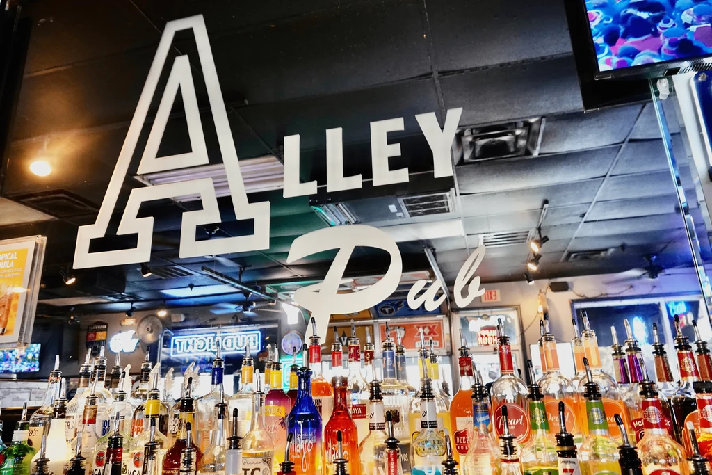 Bar interior with bright liquor bottles and prominent "ALLEY Pub" sign.