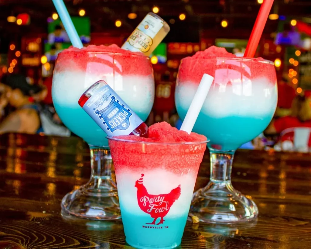 Layered red, white, blue frozen drinks with inverted liquor bottles.