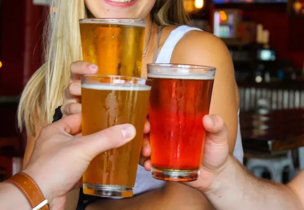 Three people cheer with cold glasses of golden and reddish beer.