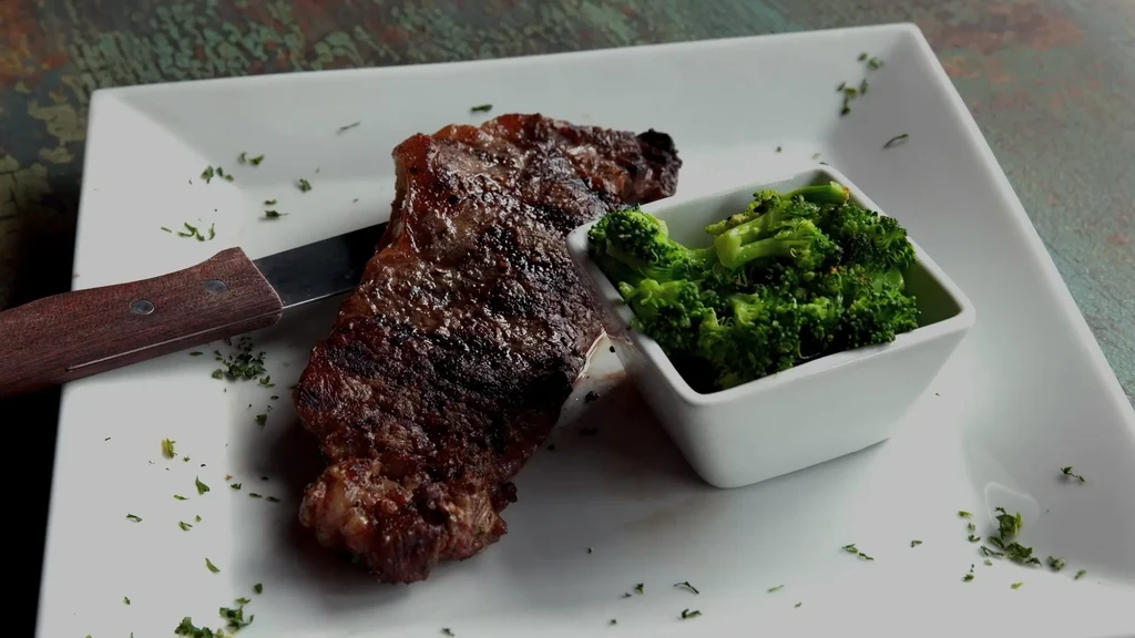 Grilled steak, steamed broccoli, and knife on a white square plate.