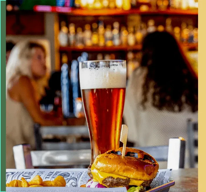 Close-up of a cheeseburger, fries, and beer at a bar.