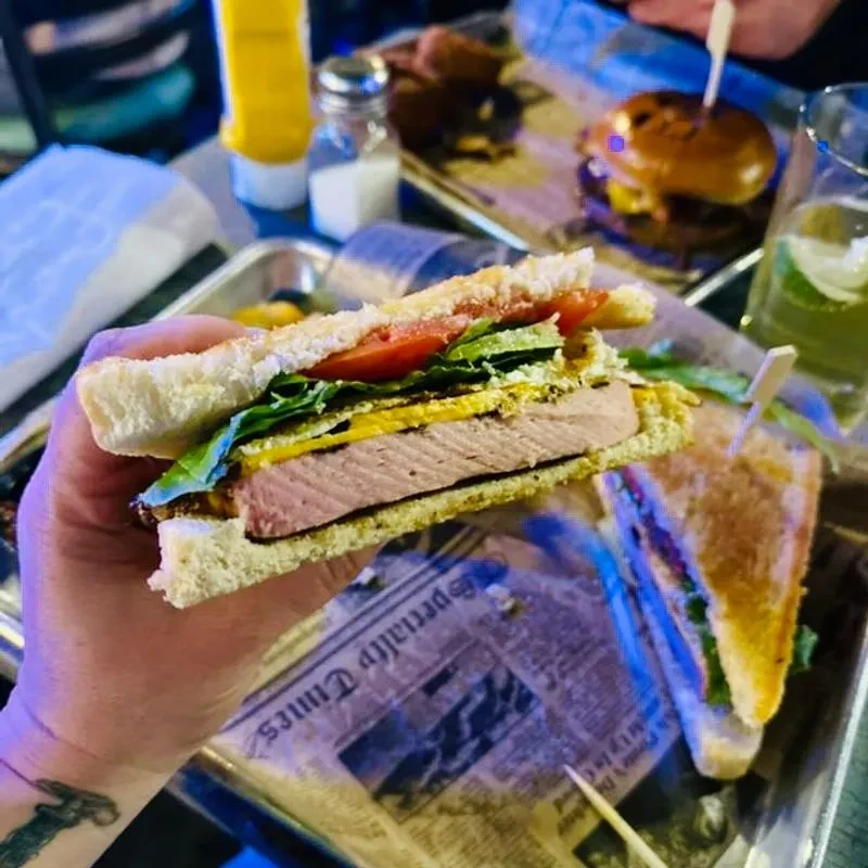 Hand holds a halved sandwich filled with meat, cheese, lettuce, and tomato.