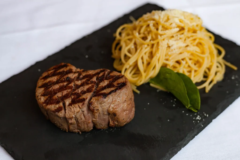 Grilled steak and spaghetti with cream sauce, cheese, and basil.