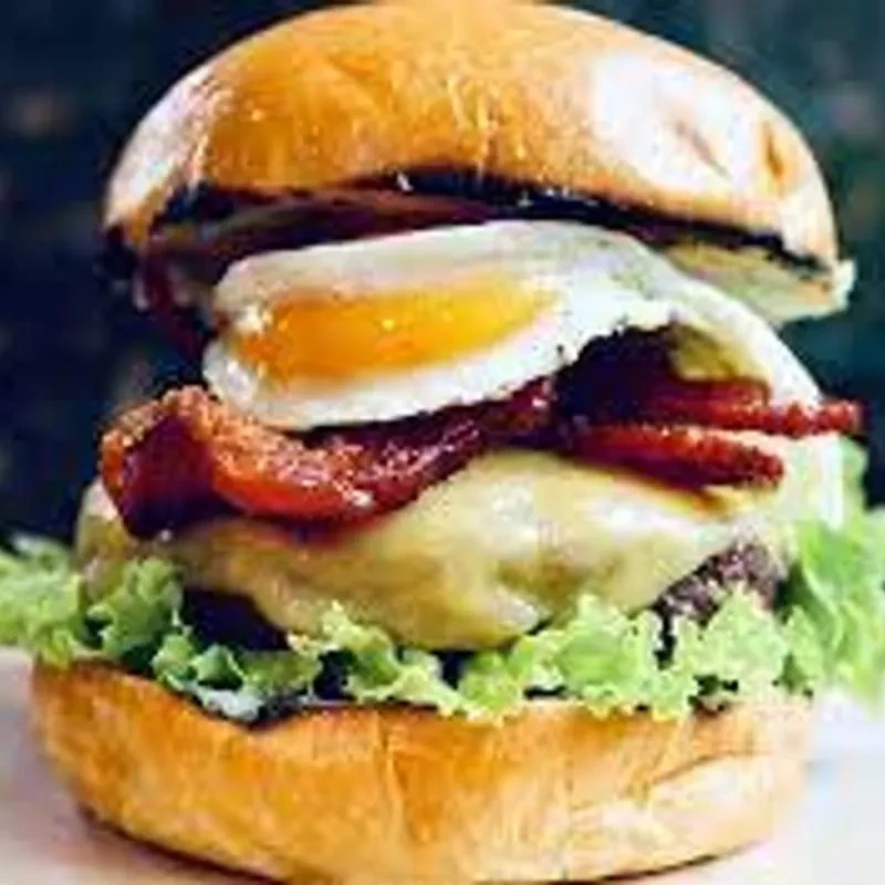 Stacked gourmet burger with egg, bacon, cheese, and lettuce.