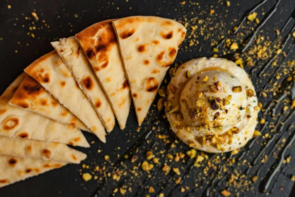Flatbread and pistachio-topped creamy dish on a dark surface.