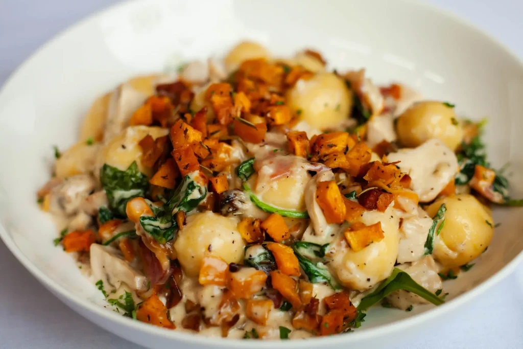 Close-up of creamy gnocchi with spinach, roasted squash, and herbs.