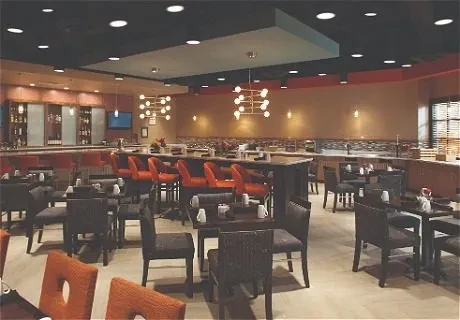Modern restaurant interior with orange bar stools and dining tables.