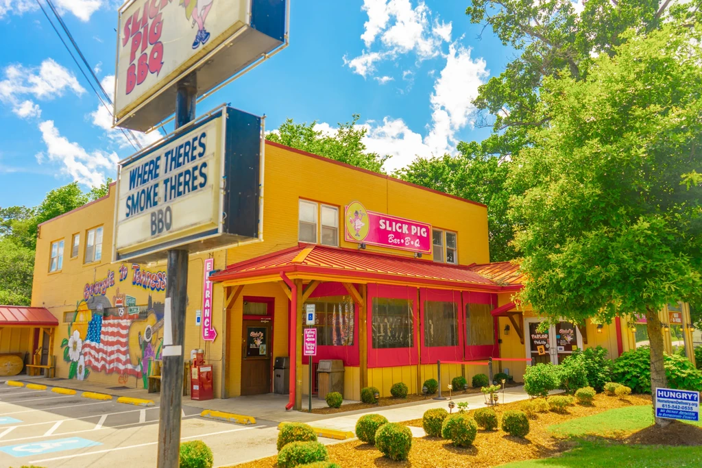Yellow Slick Pig BBQ restaurant with red roof, trees, and logo sign.