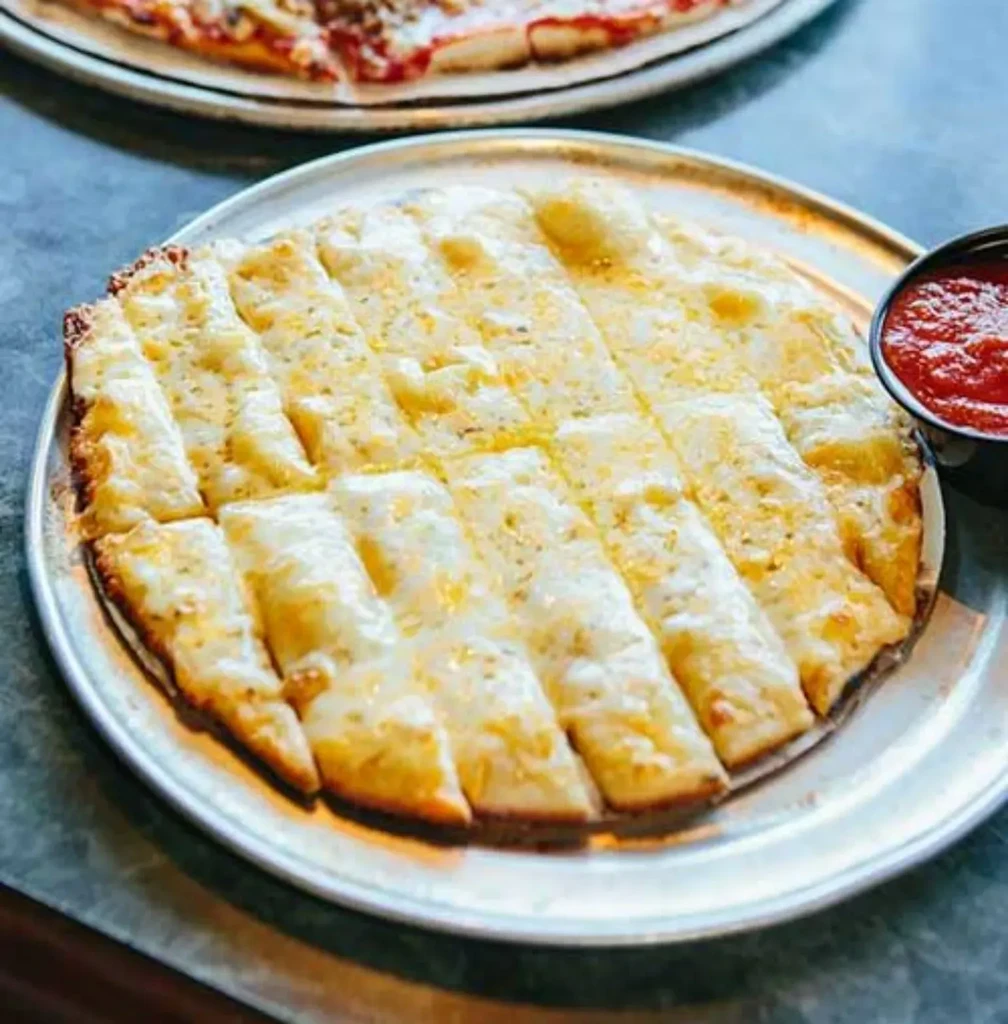 Rectangular cheesy breadsticks with melted cheese and marinara sauce.