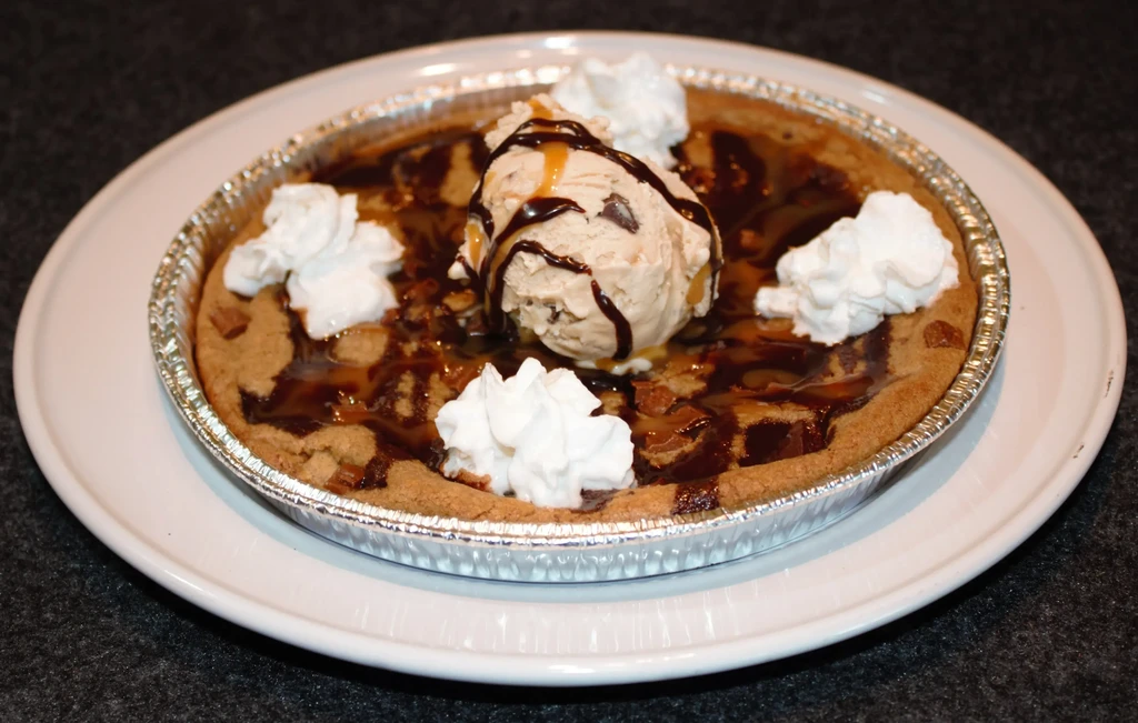 Close-up of warm cookie skillet with ice cream, sauces, and whipped cream.