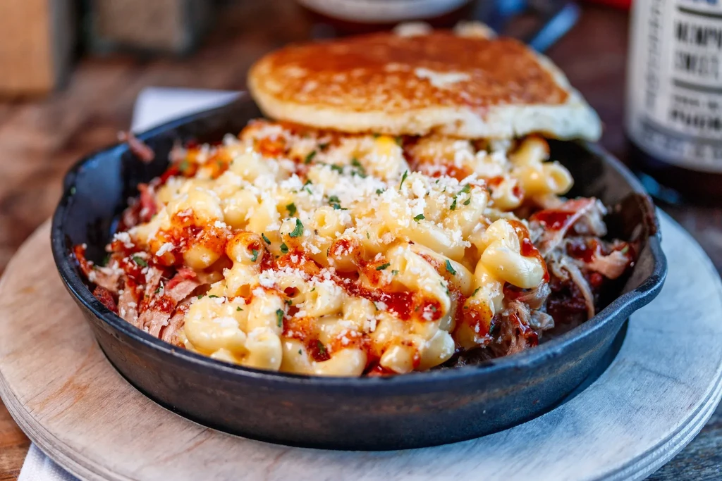 Skillet mac and cheese topped with pulled meat, sauce, and a pancake.