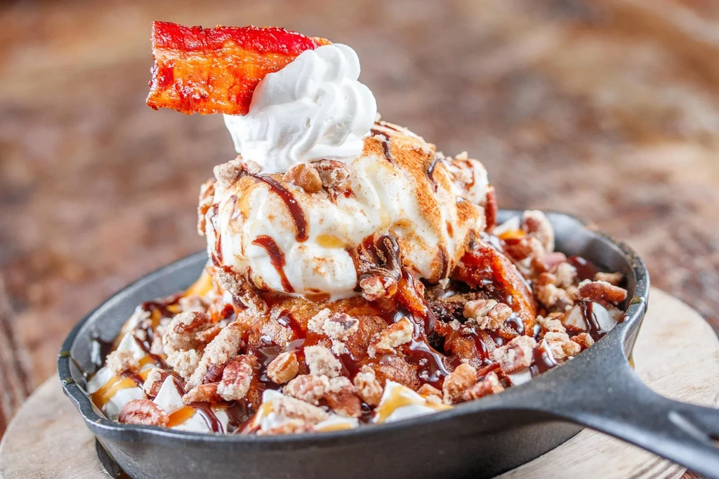Warm skillet dessert with ice cream, candied bacon, nuts, and sauces.