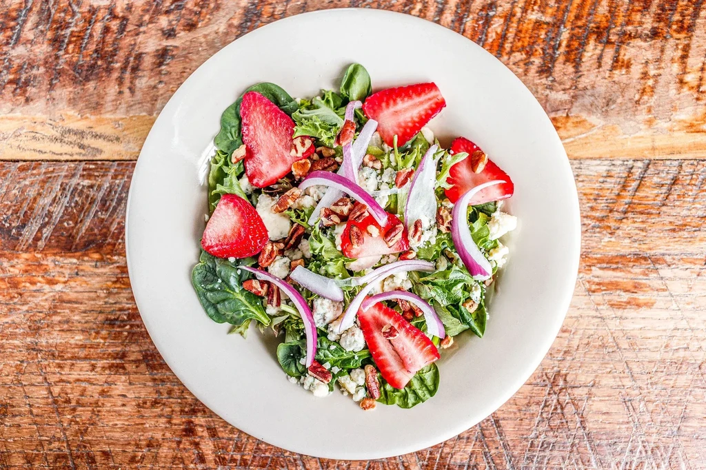 Vibrant green salad with strawberries, red onion, cheese, and pecans.