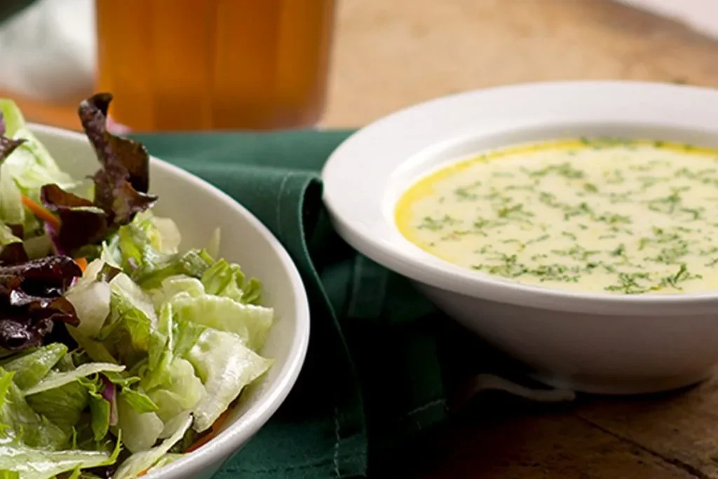 Two bowls: green salad and creamy herb soup on a wooden table.