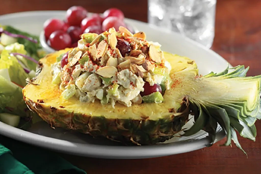 Pineapple bowl filled with creamy salad, topped with almonds and spice.