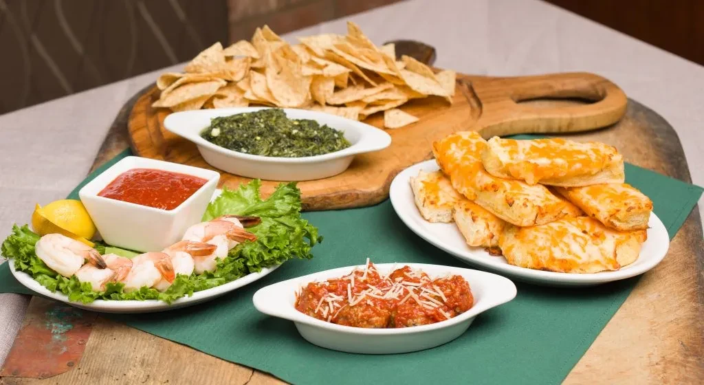Appetizer spread featuring shrimp cocktail, spinach dip, cheesy breadsticks, and meatballs.