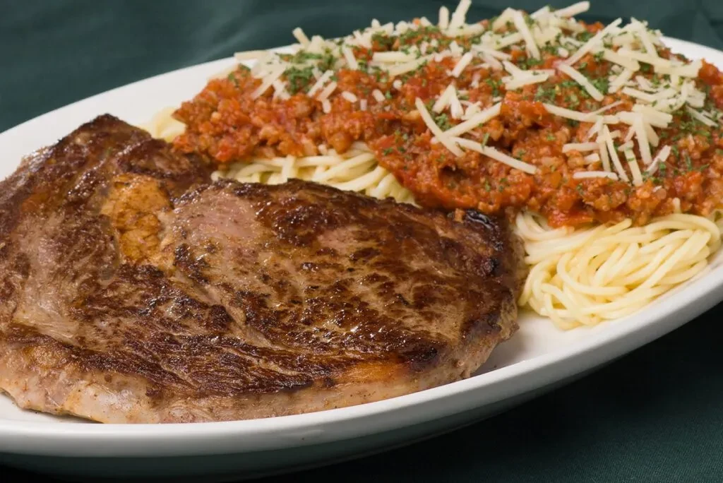 Seared steak and spaghetti with meat sauce, cheese on white plate.
