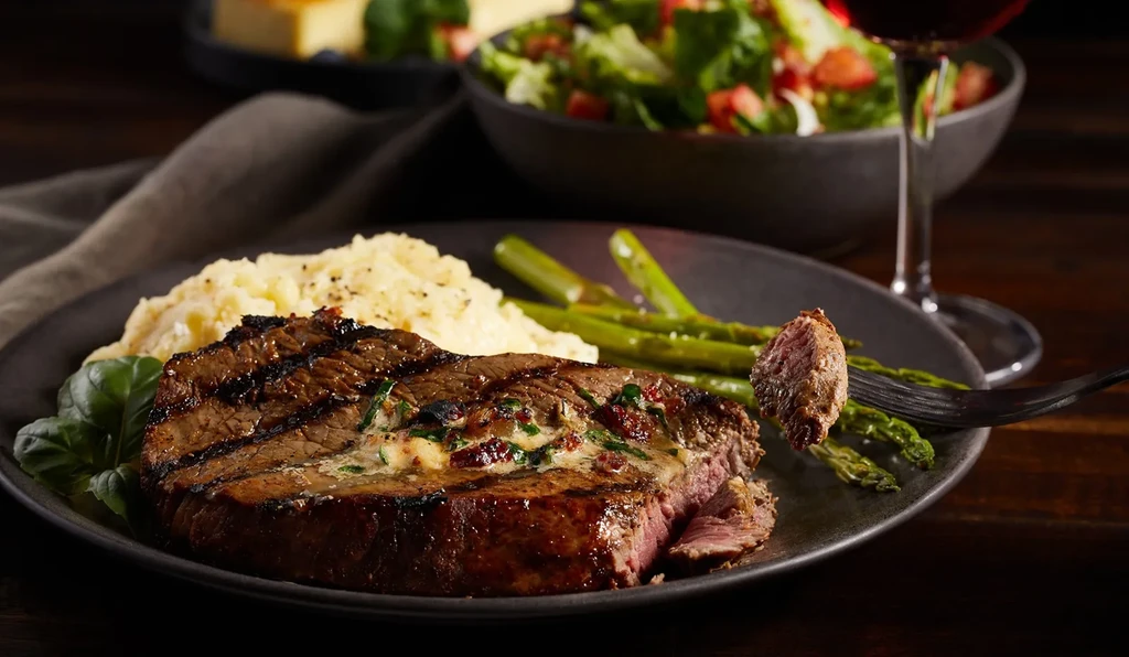Grilled medium-rare steak, mashed potatoes, and asparagus on a dark plate.