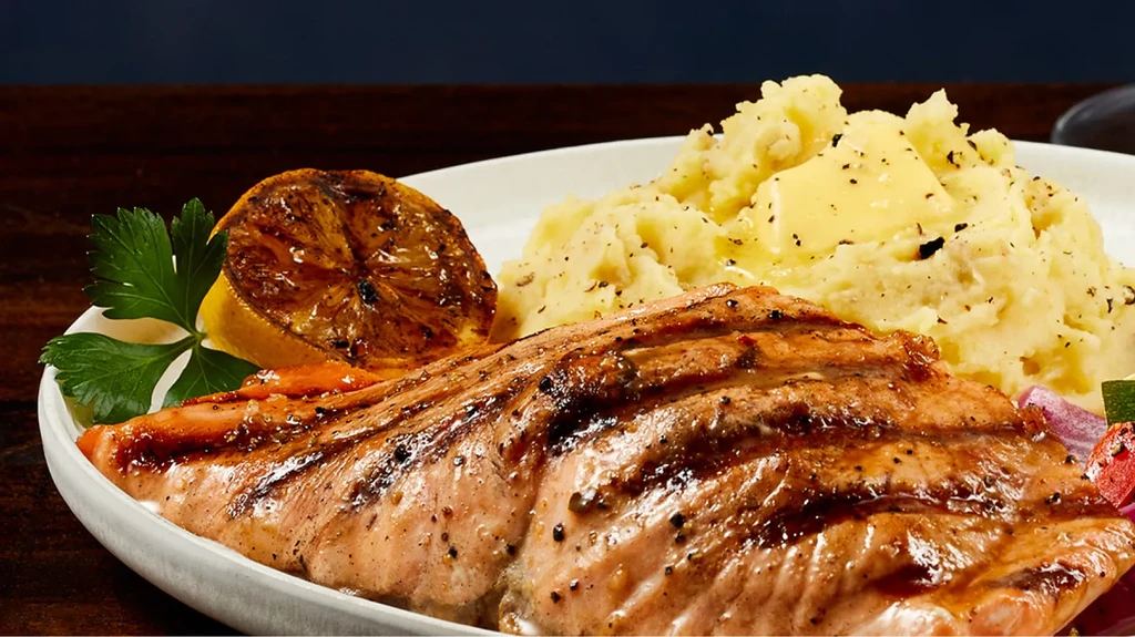 Grilled salmon fillet with mashed potatoes, lemon, and parsley.