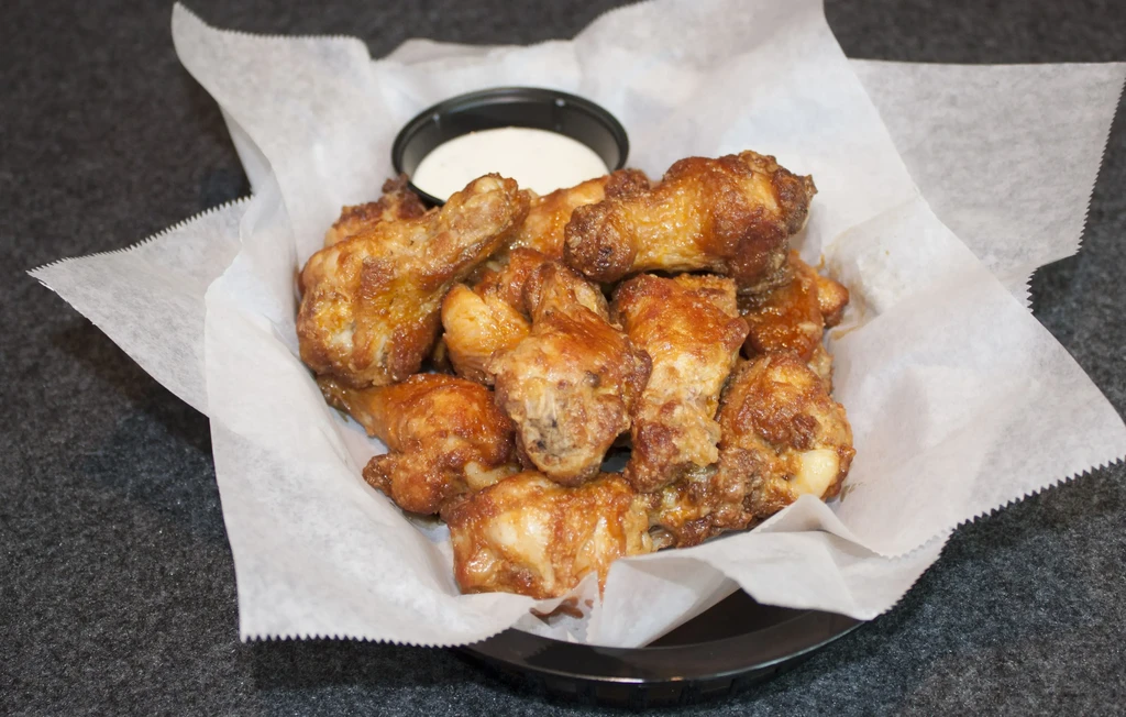 Golden-brown crispy chicken wings in a basket with white dipping sauce.